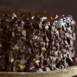 布朗尼层蛋糕上覆盖着饼干面团糖霜，巧克力糖浆在质朴的木制蛋糕架上撒在上面。