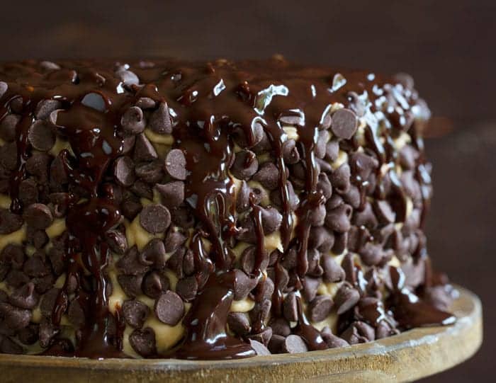 布朗尼层叠蛋糕上覆盖着饼干面团，上面撒着巧克力糖浆，放在一个质朴的木制蛋糕架上。