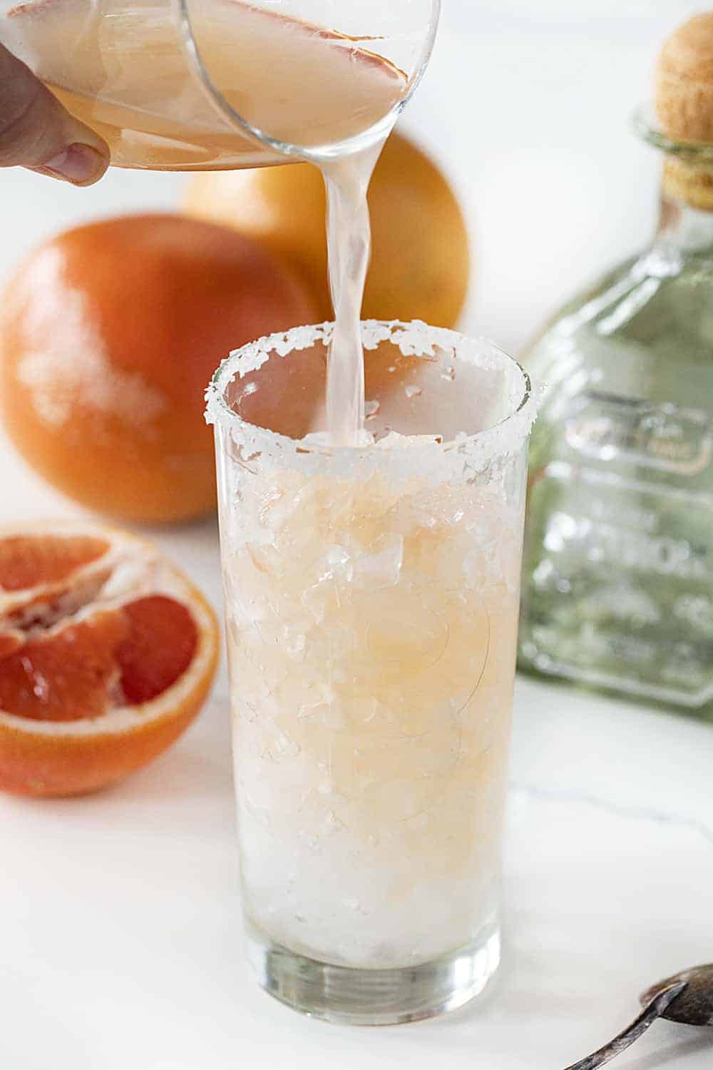 把葡萄柚倒进高脚杯里，制作帕洛玛鸡尾酒