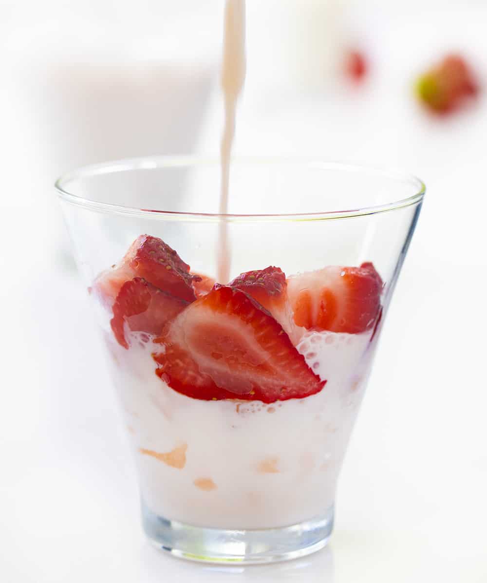 将牛奶倒入加草莓和冰的草莓和奶油牛奶杯中