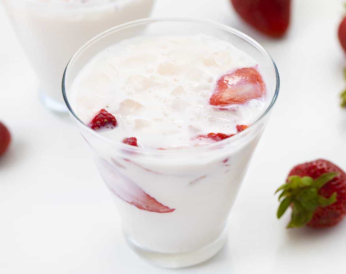 一杯草莓和奶油牛奶，周围有草莓